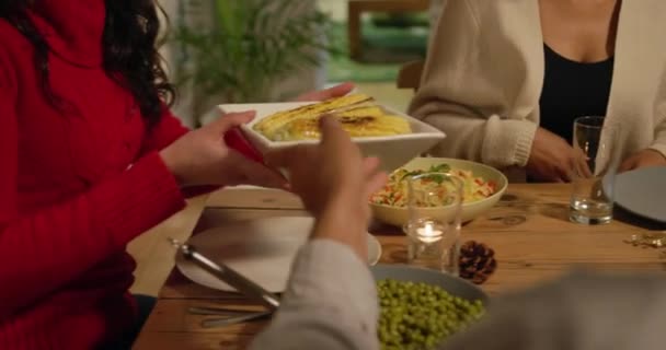 Mid section of a group of young adult multi-ethnic male and female friends sitting around a table holding dishes and serving Thanksgiving dinner at home together - Imágenes, Vídeo