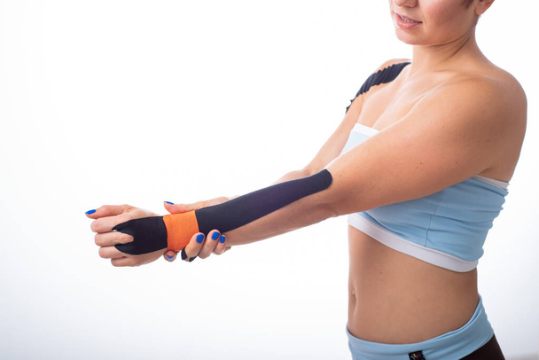 A female athlete puts a kineziotape on her wrist. Kineziology, alternative treatment for injuries of joints and tendons. Physiotherapy of chronic inflammation of the joints of a womans arm. - Fotó, kép