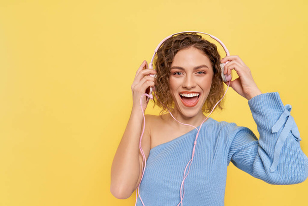 Girl holding headphones smiling, posing in studio. - Фото, изображение