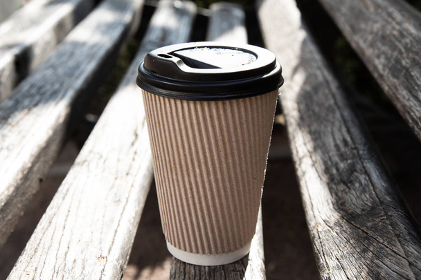Uma xícara de café de papel com tampa em um banco
 - Foto, Imagem