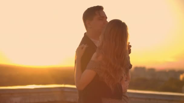 Een man en een verliefde vrouw dansen op het dak van een gebouw bij zonsondergang kijkend naar elkaar - Video