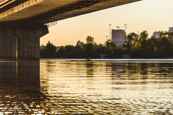 Pont sud, Kiev, Ukraine. Pont de Kiev sur la rivière Dniepr au soleil couchant. Un homme sur un bateau à rames entre les supports du pont
 - Photo, image