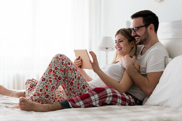 Young attractive couple using together digital tablet in bedroom - Foto, imagen