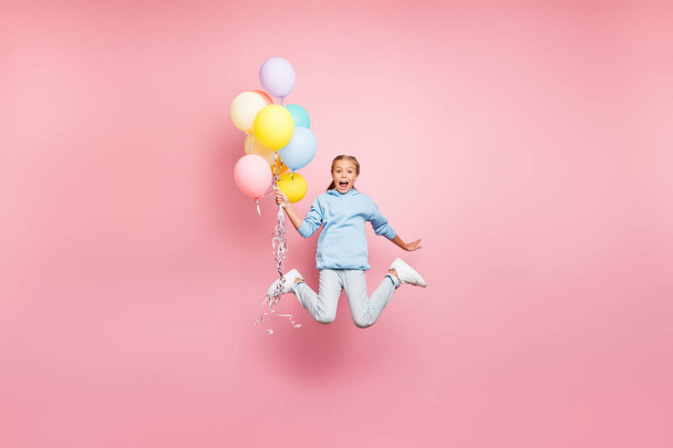 Full length body size photo of cheerfu positive cute nice screaming funny comic girl holding balloons with hands shouting flying jumping in blue sweatshirt sweater hoodie jeans denim isolated pastel - Zdjęcie, obraz