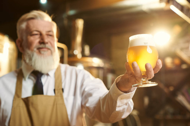 Positive brewer holding beer glass with foam. - Foto, Imagen