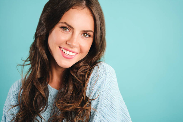 Портрет великолепной улыбающейся девушки в уютном свитере, счастливо смотрящей в камеру на синем фоне
 - Фото, изображение