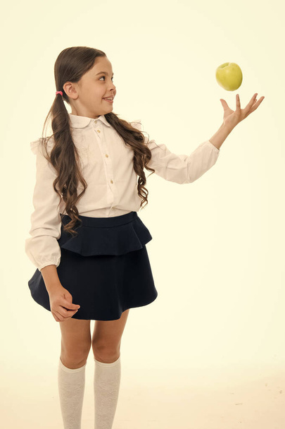 Child schoolgirl wear formal uniform hold apple. Girl cute pupil hold apple fruit stand on white background. Kid happy hold apple. School snack concept. Healthy nutrition diet. Apple vitamin snack - Photo, Image