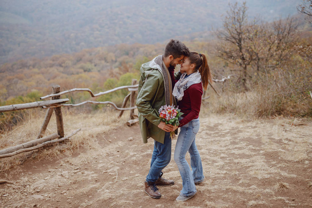 Aranyos multikulturális pár szerelmes flörtöl, miközben ősszel a természetben állnak. Egy férfi csokrot ad a barátnőjének.. - Fotó, kép