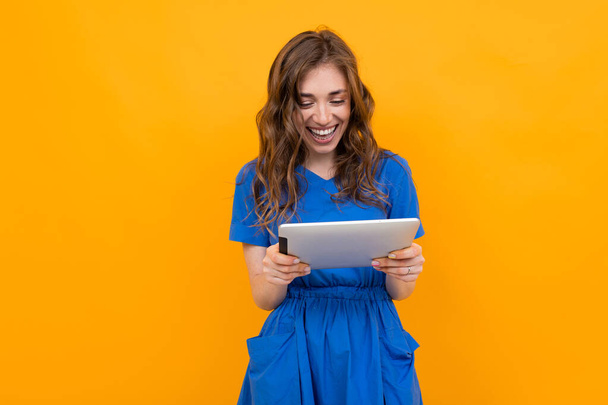 Женщина в платье позирует с цифровым планшетом на оранжевом фоне
   - Фото, изображение