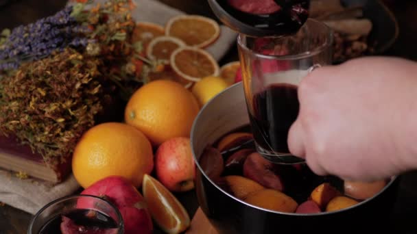 Ręce człowieka wlewają grzane wino do szklanego kubka. Świeże cytryny, pomarańcze, granaty i suszone zioła w tle. Para z wina szybuje nad rondlem. Widok z góry. - Materiał filmowy, wideo