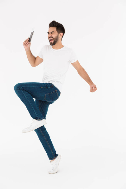 Full length image of excited young man holding cellphone and dancing - Zdjęcie, obraz