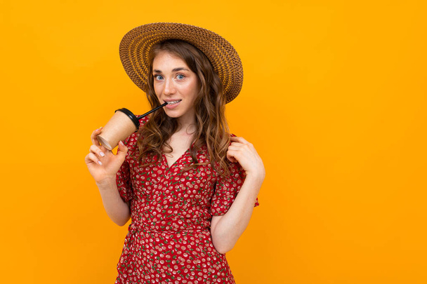 Nainen kahvia yllään mekko ja olki hattu poseeraa vastaan oranssi
 - Valokuva, kuva