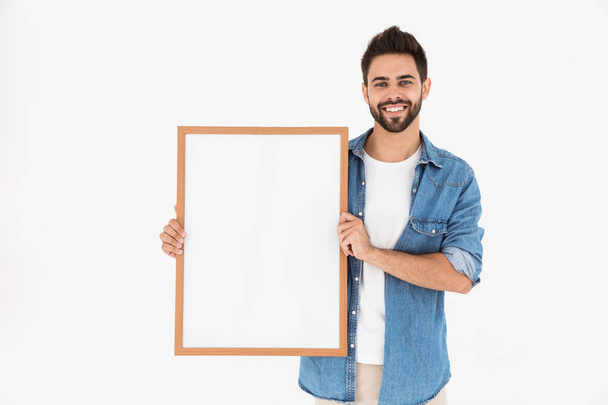 Image of young bearded man holding empty placard in frame for copyspace text and smiling - Fotoğraf, Görsel