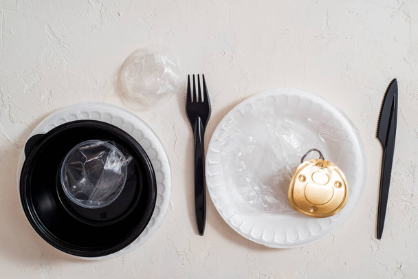 Ecology versus plastic. The concept of serving instead of food in a restaurant plastic trash. Plastic disposable tableware, bags. can covers on a black napkin and on a white table - Photo, image