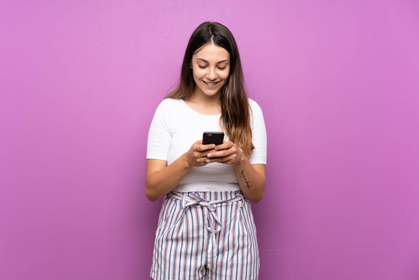 Mujer joven sobre fondo púrpura aislado enviando un mensaje con el móvil - Foto, imagen