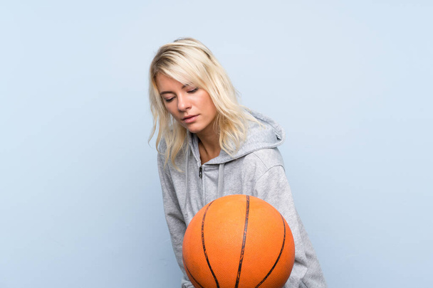 Young blonde woman over isolated background with ball of basketball - 写真・画像