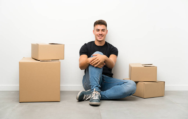 Handsome young man moving in new home among boxes with surprise facial expression - Foto, Imagem
