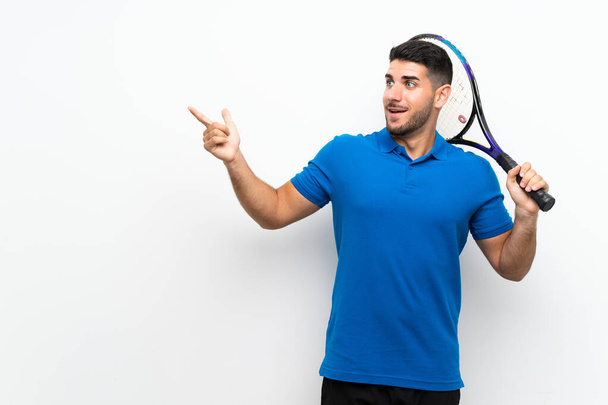 Handsome young tennis player man over isolated white wall surprised and pointing finger to the side - Foto, afbeelding