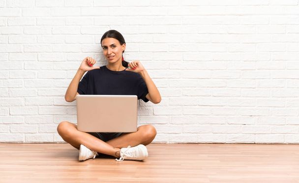 Молода жінка з ноутбуком, сидячи на підлозі, пишається і задоволена собою
 - Фото, зображення
