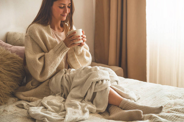 Kodikas syksyn talvi-ilta. Nainen juo kuumaa teetä ja rentoutuu kotona
.  - Valokuva, kuva