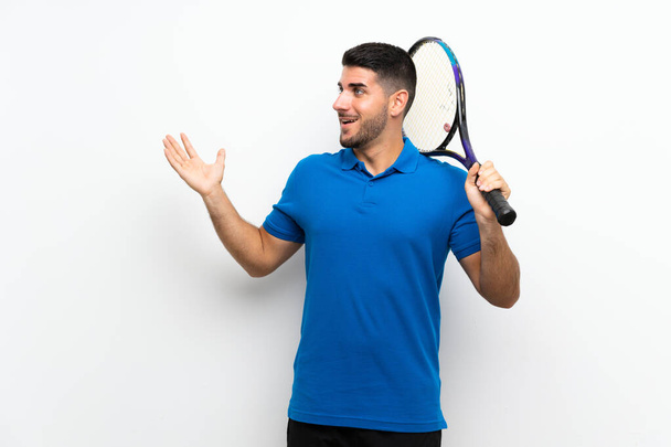Guapo joven jugador de tenis hombre sobre pared blanca aislada con la expresión facial sorpresa
 - Foto, imagen