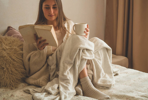 gemütlicher Herbstwinterabend. Frau trinkt heißen Tee und liest Buch.  - Foto, Bild