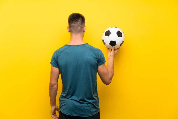 Bonito jovem jogador de futebol homem sobre isolado fundo amarelo na posição de trás
 - Foto, Imagem