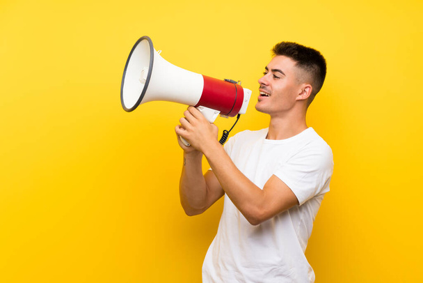 Young handsome man over isolated yellow background shouting through a megaphone - Фото, изображение