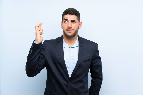 Handsome man over isolated blue background with fingers crossing and wishing the best - Foto, Imagem