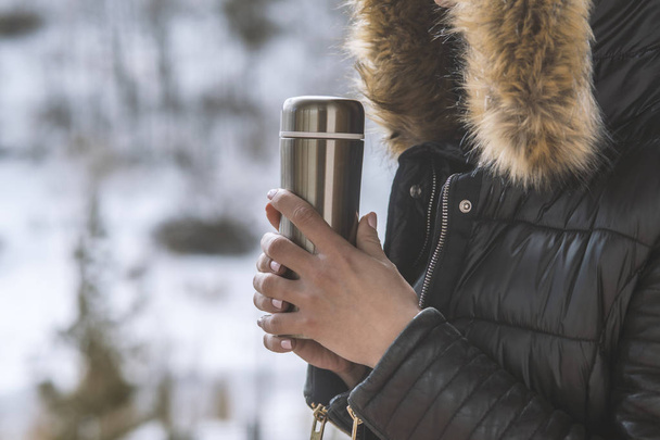 hot tea or coffee out of thermos in woman hands  on winter fores - Foto, afbeelding
