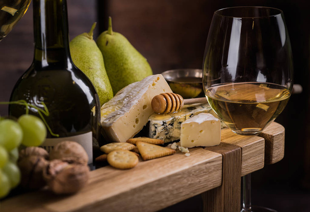 Cheese plate. With a glass of white wine, cheese, honey, pears and grapes. - Foto, afbeelding
