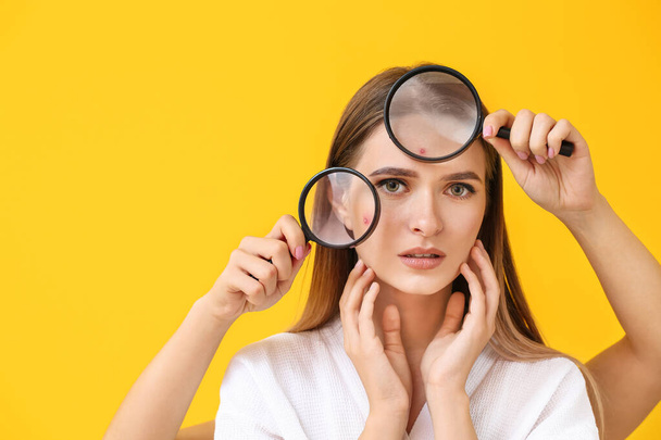 Portrait of young woman with acne problem and hands with magnifying glasses on color background - 写真・画像