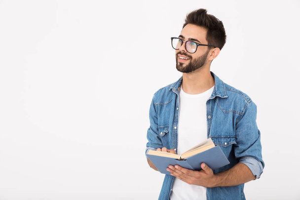 Image of young smart man wearing eyeglasses holding book and looking aside at copyspace - Foto, Bild