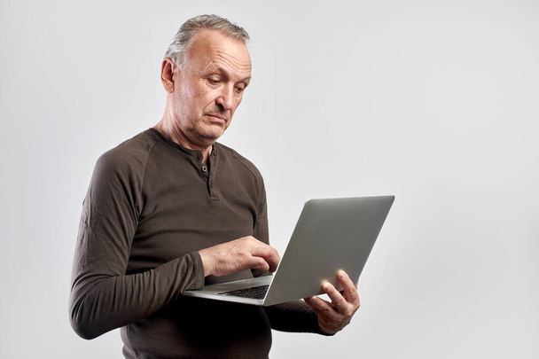 Stylish elderly man with laptop in hands pays for services and buys goods over the Internet with home delivery isolated on white background, online store - Photo, image