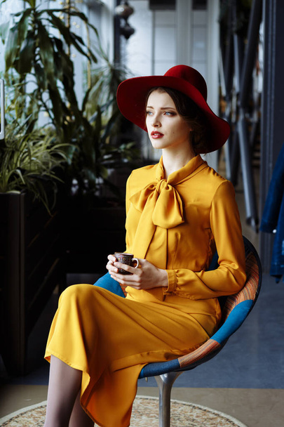 girl in a cafe with a cup of coffee and a hat.portrait of sensual young girl wearing floppy hat and blouse with bow. Beautiful brunette woman in cafe holding cup of coffee - Foto, immagini