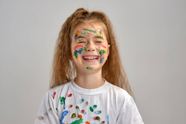 Menina em t-shirt branca, com cara pintada está fazendo grelhas ao posar isolado em branco. Estúdio de arte. Close-up. - Foto, Imagem