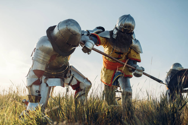 Средневековые рыцари в доспехах и шлемах сражаются мечом и топором. Бронированный древний воин в доспехах позирует на поле боя
 - Фото, изображение
