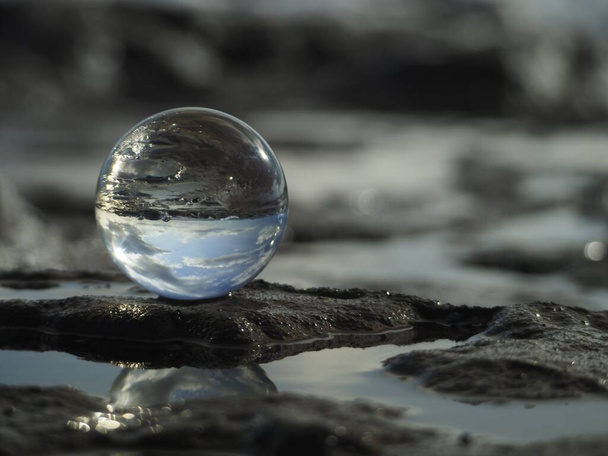 Close shot of a glass sphere reflecting the water in the middle of the rocks under a blue sky - Фото, зображення