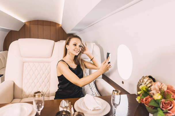 beautiful young girl in the cabin of a business class airplane with a phone in her hands comfortable luxury travel - 写真・画像