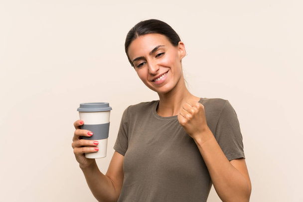 Νεαρή γυναίκα κρατώντας ένα take away καφέ γιορτάζοντας μια νίκη - Φωτογραφία, εικόνα
