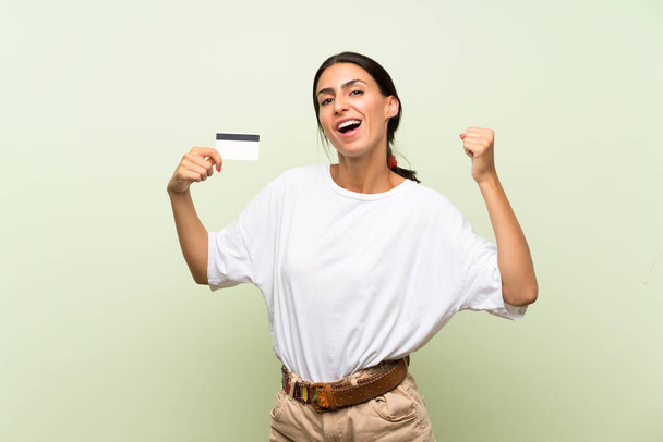 Mujer joven sobre fondo verde aislado sosteniendo una tarjeta de crédito
 - Foto, imagen