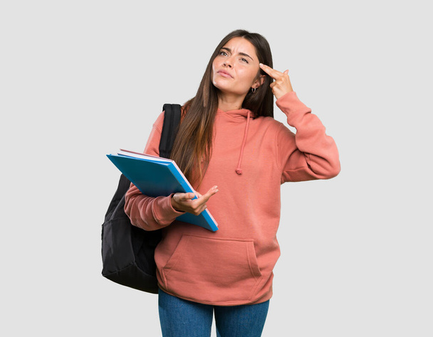 Jonge student vrouw met notitieboekjes met problemen het maken van zelfmoord gebaar over geïsoleerde grijze achtergrond - Foto, afbeelding