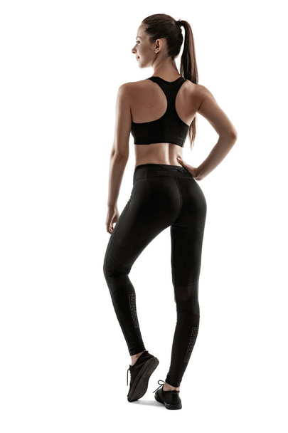 Brunette donna in leggings neri, top e sneakers è in posa isolata sul bianco. Fitness, palestra, stile di vita sano. Lunghezza totale. - Foto, immagini