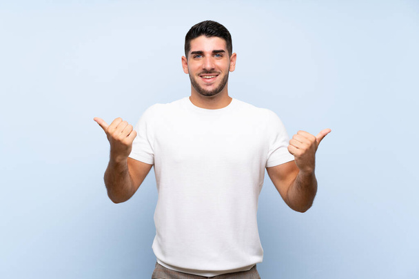 Blanke knappe man over geïsoleerde blauwe achtergrond met duimen omhoog gebaar en glimlach - Foto, afbeelding