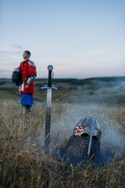 Kılıç yere saplandı ve metal şövalye miğferi, hiç kimse, büyük savaşçı sembolü tarlada - Fotoğraf, Görsel