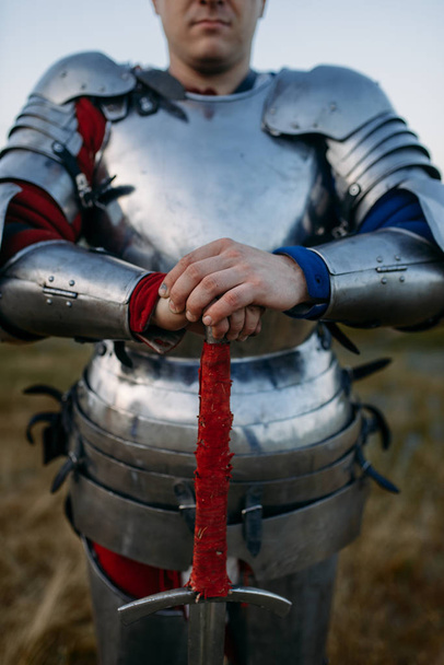 Medieval knight in metal armor holds sword, great battle. Armored ancient warrior in armour posing in the field - Foto, afbeelding
