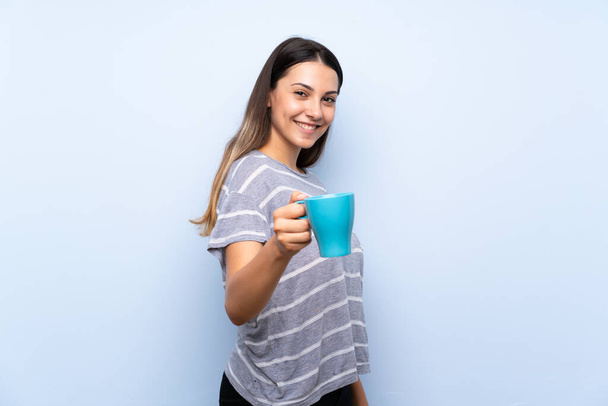 Młoda brunetka kobieta na białym tle niebieskie przytrzymanie gorącej filiżanki kawy - Zdjęcie, obraz