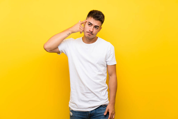 Young handsome man over isolated yellow background making the gesture of madness putting finger on the head - Photo, Image