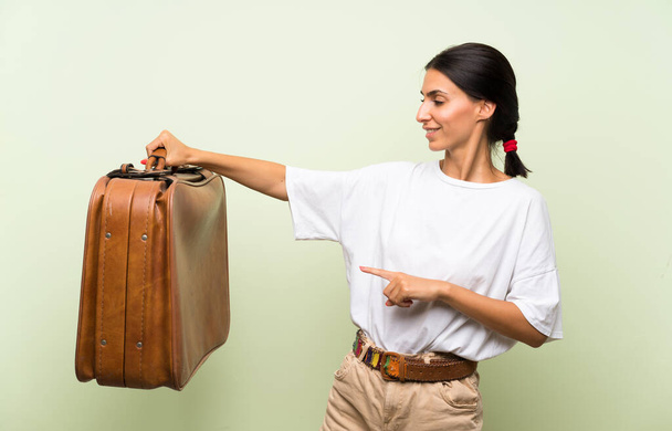 Young woman over isolated green background holding a vintage briefcase - Photo, Image