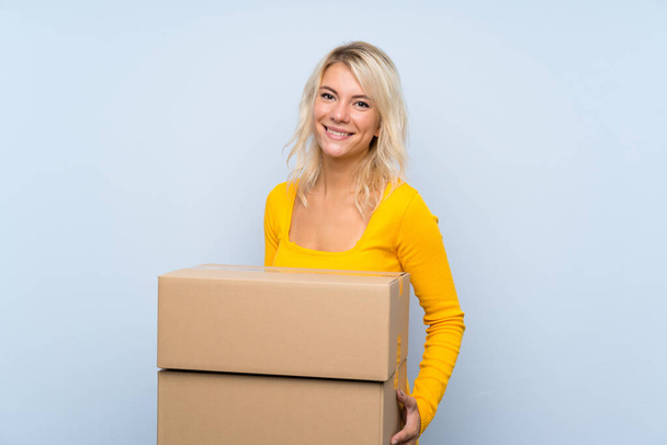 Jonge blonde vrouw over geïsoleerde achtergrond met een doos om het te verplaatsen naar een andere site - Foto, afbeelding
